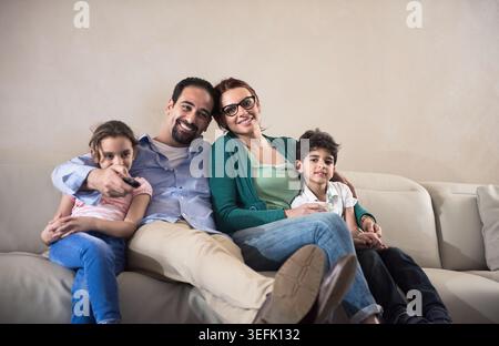 Famille arabe moderne du moyen-Orient se relaxant ensemble sur le canapé tout en regardant la télévision à la maison Banque D'Images