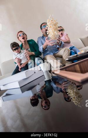 Famille moderne du moyen-Orient regardant un film ensemble à la maison avec pop-corn volant dans le salon surprise Banque D'Images