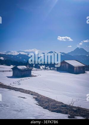 Vieilles cabanes alpines en bois entourées de neige fraîche, baignées de soleil avec des montagnes majestueuses Dolomites en arrière-plan, Luson, Bolzano Banque D'Images