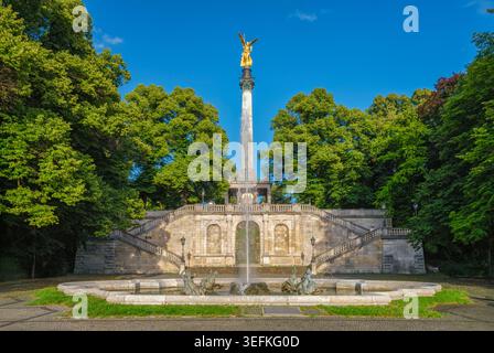 La statue dorée de l'Ange de la paix au sommet d'une haute colonne avec un grand escalier en pierre et une fontaine à Munich, Bavière, Allemagne au coucher du soleil. Banque D'Images