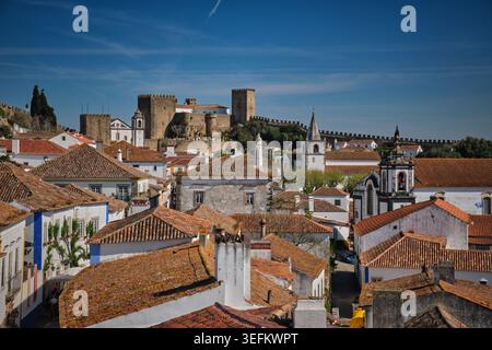 Vue surélevée plus proche d'Obidos, Portugal, avec des toits superposés, des tours d'église et le château dominant la ligne d'horizon au-dessus de la vieille ville. Banque D'Images