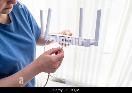 Gros plan d'une personne en chemise bleue connectant un câble réseau à un routeur sans fil. Ce cliché représente l'installation internet à domicile, le tro technique Banque D'Images