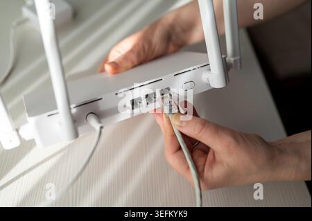 Gros plan détaillé d'une personne connectant un câble réseau à un routeur sans fil doté d'antennes. Concept de configuration Internet haut débit, su technique Banque D'Images
