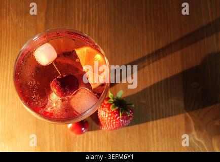 Spritzer de fruits rouges dans un verre avec de la glace, cerise et tranche d'orange, frais et pétillant sur une table en bois vibrante, rafraîchissante boisson d'été parfaite pour PA Banque D'Images
