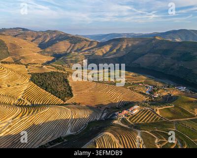 Des collines et des vignobles en terrasses entourent le fleuve Douro dans cette vue aérienne du coucher de soleil depuis la vallée du Douro au Portugal. Banque D'Images
