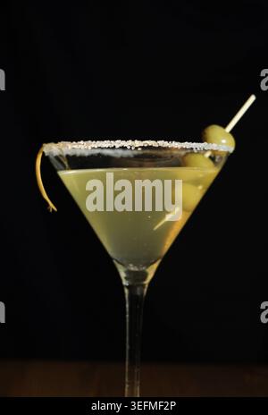 Cocktail Martini dans un verre clair glacé avec des olives vertes, une touche de citron et un bord salé de sucre sur un fond sombre, boisson classique élégante pour le cauchemar Banque D'Images