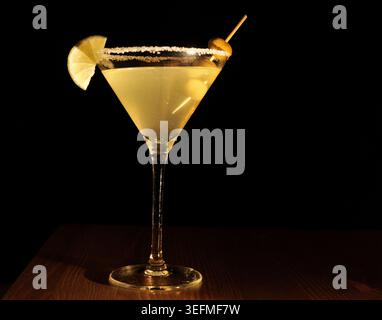 Cocktail Margarita avec un bord salé, garni d'un coin de citron vert frais et d'olives cocktail, debout sur une surface en bois foncé contre un backgro noir Banque D'Images