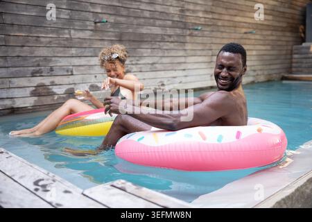 Divers amis flottant sur des flotteurs dans la piscine privée, tenant un verre de boisson et portant des lunettes de soleil Banque D'Images