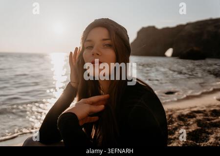 Femme, coucher de soleil, portrait de plage d'une jeune voyageuse réfléchie portant un bonnet au bord de la mer pendant l'heure d'or. Banque D'Images