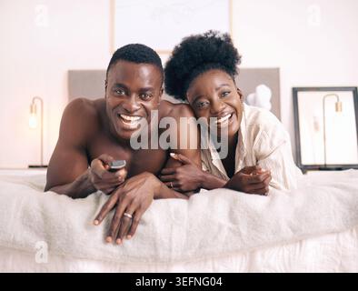 Chambre, portrait et couple regardant la télévision pour streaming, film ou film le week-end à la maison. Télécommande, télévision et homme noir et femme se détendre, sourire et Banque D'Images