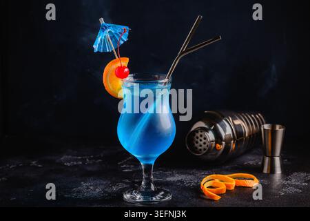 GGass de cocktail bleu lagon décoré d'orange et de cerise sur fond de comptoir de bar festif. Banque D'Images