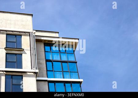 La façade de bâtiment résidentiel moderne présente des baies vitrées rythmées avec du verre bleu contre le ciel lumineux. L'architecture contemporaine met en valeur la conc. Verticale Banque D'Images