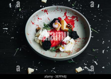 Assiette à desserts gastronomiques avec baies mélangées, fromage crémeux et herbes vertes Banque D'Images