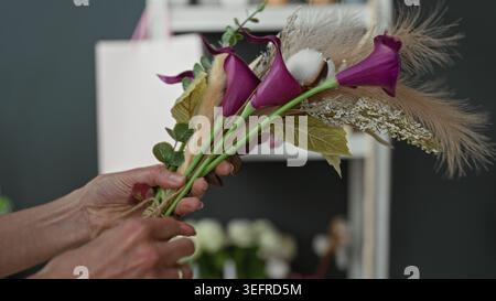 Femme fleuriste mains arranger le bouquet de calla violet avec l'herbe de pampas et l'eucalyptus et ficelle de cravate dans un studio ; artisanat calme. Banque D'Images