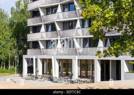 Immeuble contemporain doté de balcons inclinés, de fauteuils de café en plein air au rez-de-chaussée et de grandes fenêtres situées à côté d'arbres dans un quartier calme et verdoyant Banque D'Images