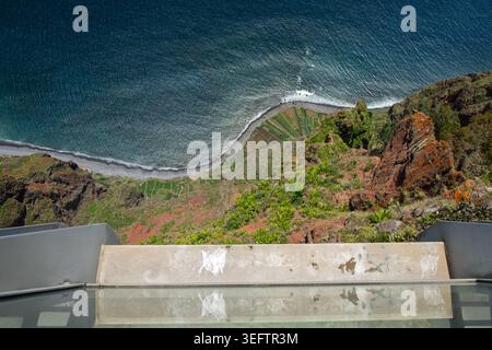 Funchal, Madère, 12 mai 2026. Vue d'en haut montrant l'océan bleu profond, une plage rocheuse et des champs en terrasses à la base de falaises vertes et rouges abruptes Banque D'Images