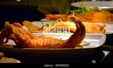 Alignez des filets de poisson panés britanniques frits avec des herbes vertes dans des assiettes blanches. Cliché authentique du restaurant. Banque D'Images