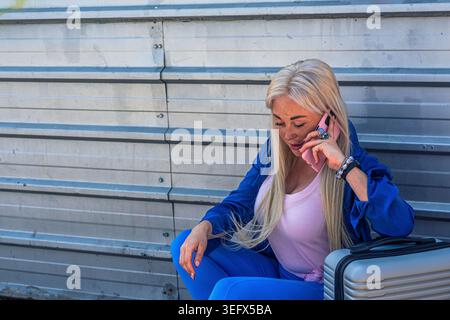 Jeune femme voyageant faisant un appel téléphonique, assise avec des bagages Banque D'Images