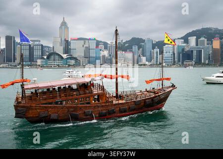 Jonque chinoise traditionnelle naviguant dans le port Victoria avec l'emblématique horizon de Hong Kong, Hong Kong Banque D'Images