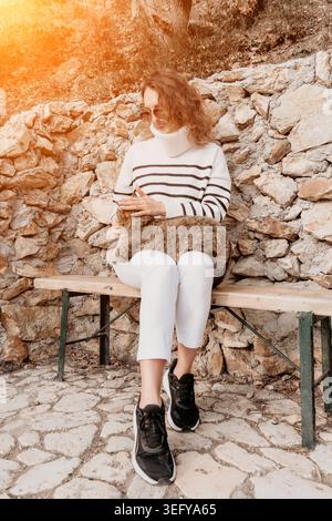 Chat femme caressant assis sur un banc à l'extérieur tout en câlant un félin tabby moelleux sous la lumière du soleil dorée chaude Banque D'Images