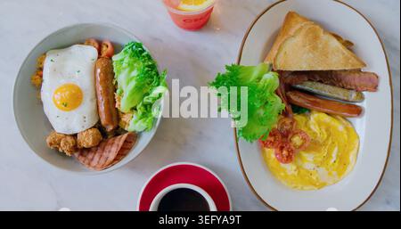 Deux assiettes de petit-déjeuner copieux avec œufs, saucisses, bacon et pain grillé servis sur une table en marbre lumineux. Délicieux concept de repas du matin. Frais, vifs et Banque D'Images