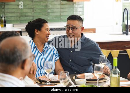 Homme asiatique senior et couple de femme mature souriant et parlant à la table à manger avec bouteille de vin Banque D'Images