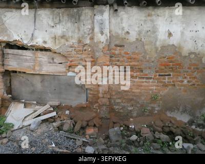 Une vue rapprochée d'un mur de briques en décomposition avec des taches de ciment usé et des planches de bois cassées. Situé dans une zone urbaine, cette structure altérée montre Banque D'Images