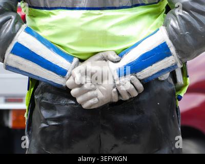 Gros plan d'un mannequin habillé comme un policier de la circulation avec les mains croisées derrière le dos, portant un gilet réfléchissant jaune fluo et bleu-stri Banque D'Images