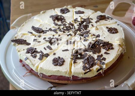 Gâteau fait maison avec gelée de cerise, crème fouettée, et décorations de chocolat noir sur un plateau en plastique, la cuisson d'un dessert pour une fête décontractée en famille ou f Banque D'Images