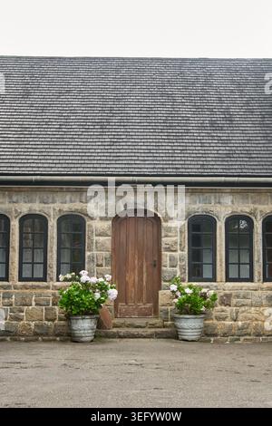façade de bâtiment en pierre avec porte arquée en bois brun et toit, fenêtres à multiples vitres encadrées noires et pots de fleurs, vue avant avec espace de copie, traditionnel Banque D'Images