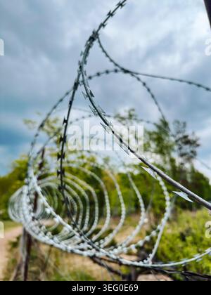 Des clôtures de fil de fer barbelé entourent un espace vert par une journée nuageuse dans un endroit rural dans la campagne Banque D'Images