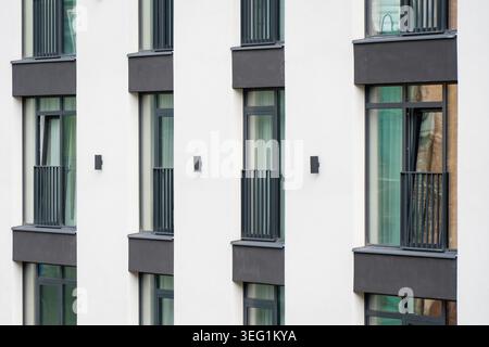 Plan architectural rapproché d'un extérieur d'immeuble nouvellement construit avec des fenêtres sombres symétriques et des rampes verticales sur un plâtre propre s. Banque D'Images