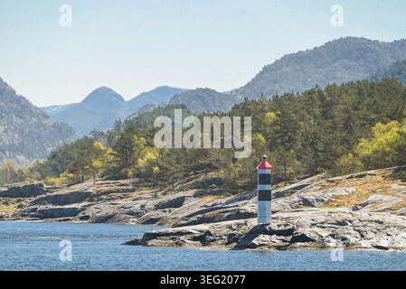 Un petit phare côtier rayé noir et blanc sur une rive rocheuse dans un fjord norvégien, en Norvège Banque D'Images
