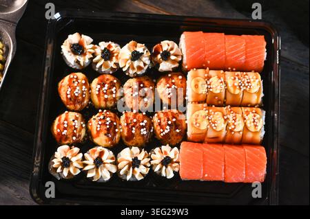 assortiment de sushis disposés en rangées soignées avec rouleaux et nigiri, morceaux de sushis garnis de saumon et de sauce, composition de fruits de mer frais sur assiette, gros plan Banque D'Images