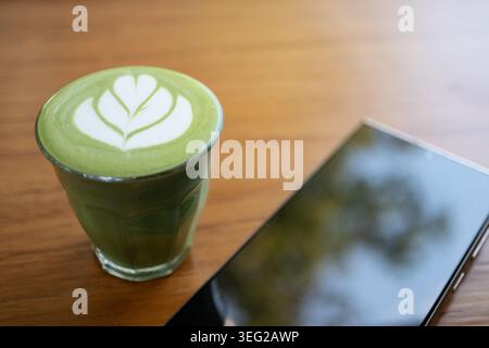 Matcha Piccolo Latte avec Leaf Latte Art en verre sur table en bois avec smartphone Banque D'Images