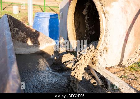 Gros plan du béton humide coulé d'un malaxeur rotatif dans une brouette sur un chantier extérieur, montrant du ciment frais, une texture de gravier et une construction Banque D'Images