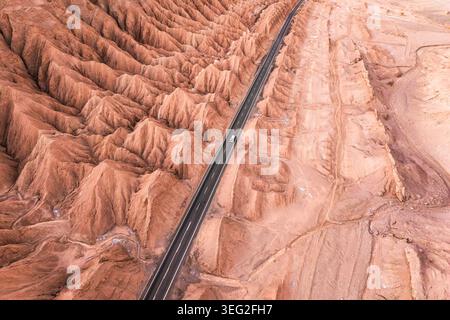 Vue aérienne par drone d'une route panoramique traversant le désert accidenté d'Atacama, au Chili, avec des crêtes de grès érodées spectaculaires et un terrain aride sous-jacent Banque D'Images