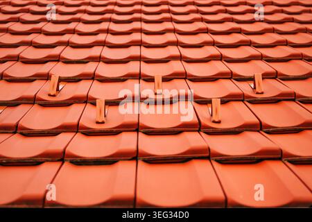 Tuiles de toiture en terre cuite texturée avec pare-neige métalliques sur le toit de la maison en pente, détails de construction et conception géométrique, mise au point sélective Banque D'Images