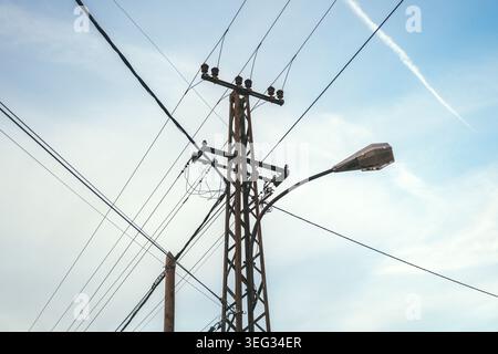 Poteau de service avec lignes électriques croisées et un lampadaire courbe placé contre un ciel bleu clair, illustrant l'infrastructure urbaine, les câbles aériens a Banque D'Images