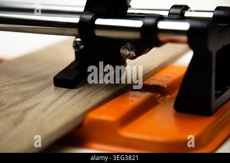 Gros plan d'un coupe-carreaux mécanique orange, qui a fixé des carreaux de céramique de couleurs en bois, au-dessus Banque D'Images