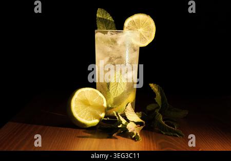 Cocktail de mojito dans un grand verre rempli de glace, de citron vert tranché et de menthe fraîche, préparé comme boisson alcoolisée pétillante et rafraîchissante sur un dos sombre Banque D'Images