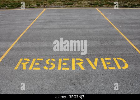 Espace de stationnement « RÉSERVÉ » clairement marqué avec des lettres jaunes en gras et des lignes de limite peintes sur de l’asphalte à côté d’un bord herbeux dans un stationnement extérieur. Banque D'Images