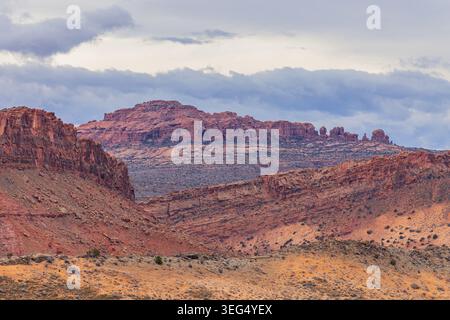 Des falaises de grès rouge érodées et des mesas en couches dominent le paysage désertique aride sous un ciel couvert. Banque D'Images