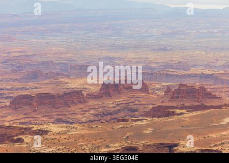 D'énormes formations rocheuses rouges en couches s'élèvent d'un vaste fond de vallée désertique qui s'estompe dans l'horizon lointain. Banque D'Images