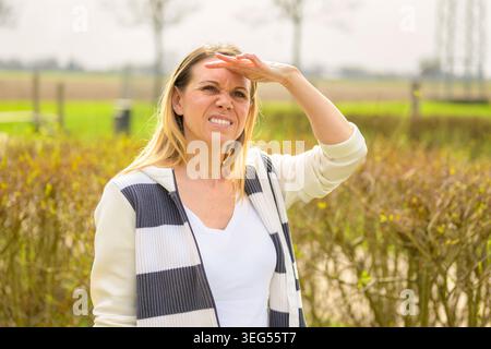 Jeune femme protégeant ses yeux de la lumière du soleil tout en se tenant à l'extérieur dans un paysage rural. Portrait de style de vie naturel représentant le soleil, Sear Banque D'Images