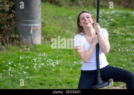 Heureuse jeune femme appréciant le moment extérieur ludique sur l'oscillation de terrain de jeu. Portrait de style de vie authentique représentant la liberté, la joie, la détente et l'insouciance Banque D'Images