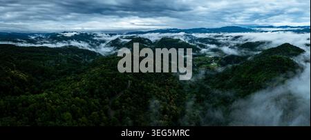 Vue panoramique sur les crêtes montagneuses reculées avec un épais brouillard de vallée de végétation tropicale et des parcelles agricoles lointaines sous un ciel couvert spectaculaire. Banque D'Images