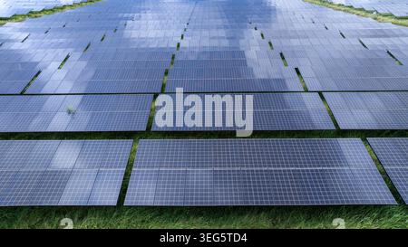 Une vue surélevée d'une ferme d'énergie solaire à grande échelle avec des rangées de panneaux photovoltaïques sur un terrain herbeux pour une production d'énergie durable. Banque D'Images