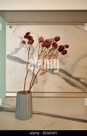 Une composition équilibrée, à hauteur des yeux, avec des branches fines et fragiles avec des baies foncées dans un vase gris cannelé. Banque D'Images