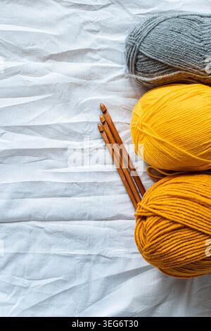 Pose à plat de crochets en bois à côté des écheveaux de fil gris et jaune sur tissu blanc froissé. Concept d'artisanat confortable fait à la main avec espace de copie pour knitt Banque D'Images